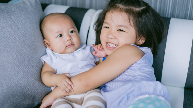 Little girl on couch holding baby