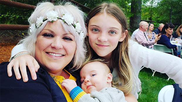 Ashley Lee holding her newborn, hugged by her older daughter