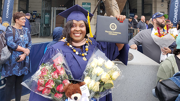 Ericka Campbell in purple graduation gown holding her diploma outside stadium