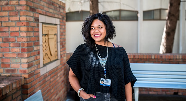 Rena Ortigoza standing near picture on brick wall, smiling Rena Ortigoza standing near picture on brick wall, smiling