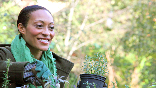 Gloria gardening, with a green scarf around her neck, smiling