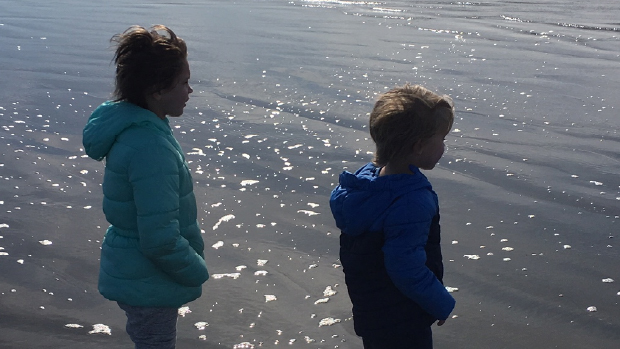 Two children playing on the beach looking out at the ocean