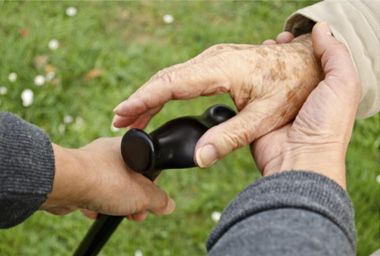 Hands of a nurse guiding the hands of an older person reach for a cane