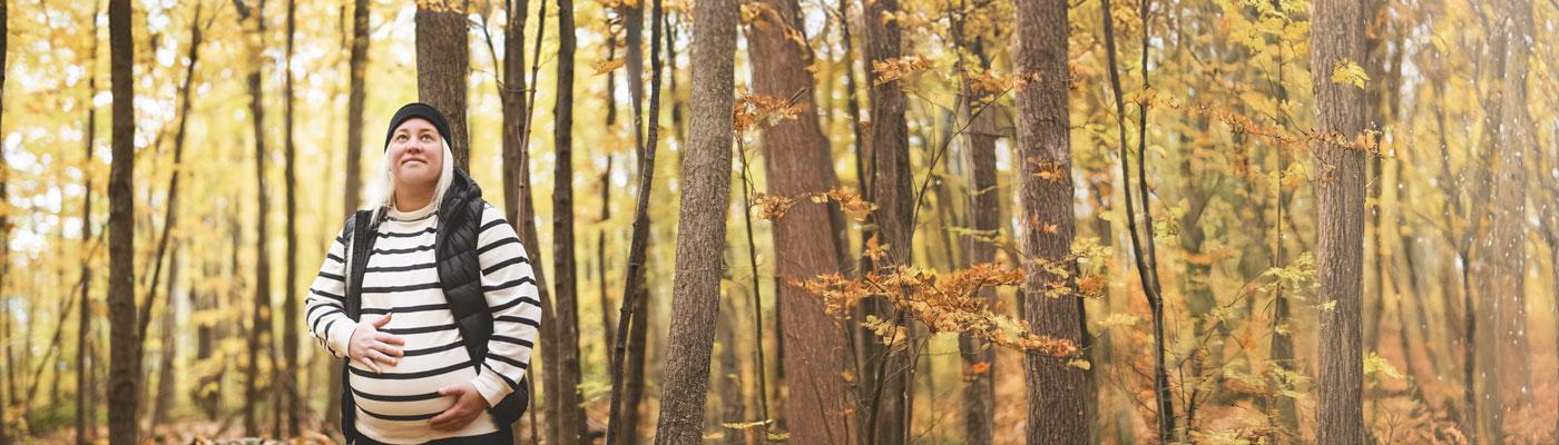 Pregnant young woman in a stripped shirt and beanie, walking through the autumn woods.