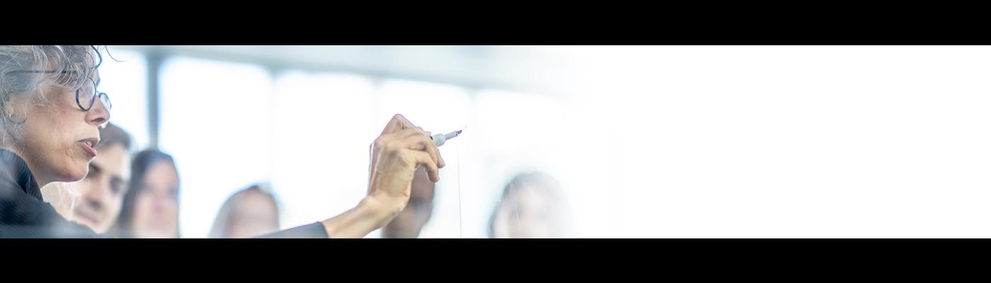 Older woman in a meeting pointing at white board with a purple marker