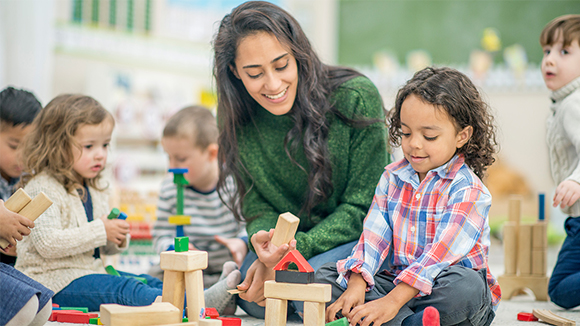 Young female teacher with kids, playing with blocks