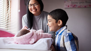 Woman and boy looking over crib smiling at baby